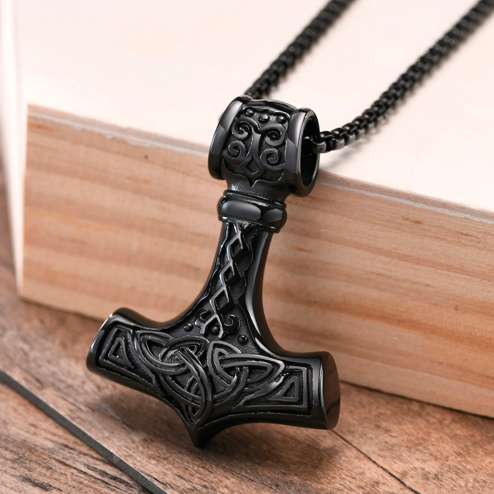 Black Thor's hammer pendant on a chain against a wooden background